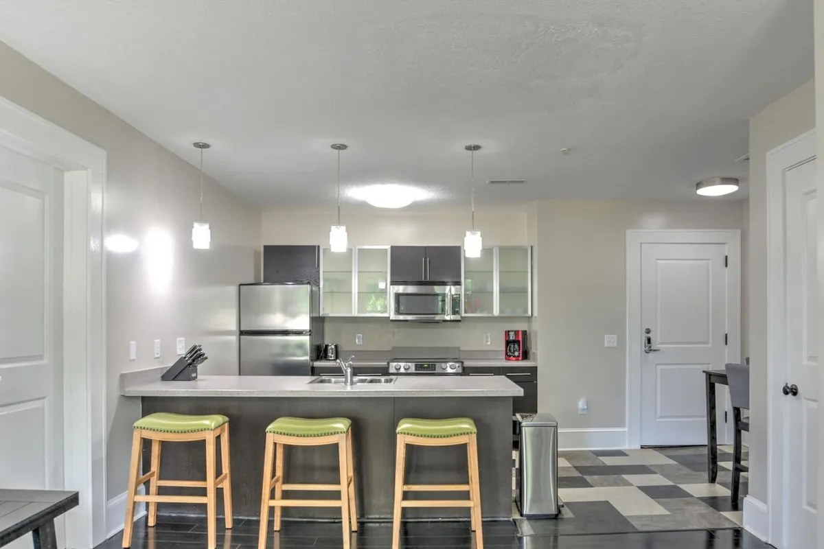 A modern kitchenette layout centered around a kitchen island with bar stools, complemented by sleek stainless steel appliances. The setup is designed for cooking, entertaining, and gathering, reflecting efficiency and style.