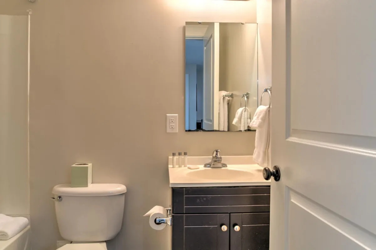 A modern, inviting bathroom with a clean sink area, mounted mirror, neatly arranged towel rack, and a pristine toilet. The space feels tidy and spa-like, perfect for relaxation and freshening up.