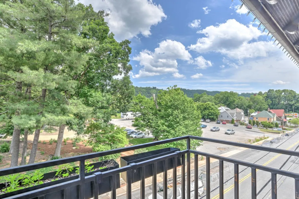 This image features a tranquil balcony scene overlooking green trees and a quiet street, with a cloudy sky enhancing the peaceful ambiance. The focus is on the outdoor space, where one could enjoy a coffee while taking in the scenery, read a book outside, or simply relax in the fresh air. The balcony railing frames the view, suggesting a serene retreat amid the neighborhood’s charm.