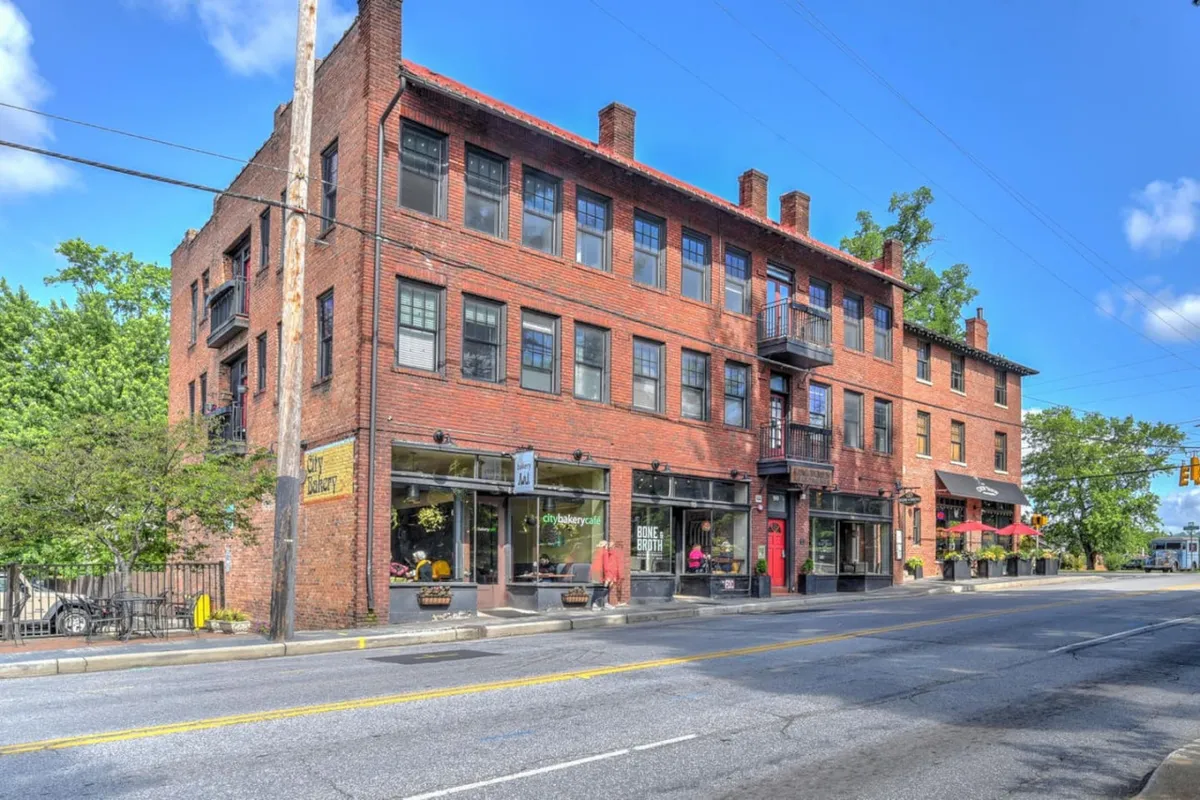 A street-level perspective of the building with its historic brick architecture, large windows, and lively outdoor seating. The image captures both the grandeur and the neighborhood context, offering a glimpse of the vibrant urban setting just outside the entryway.