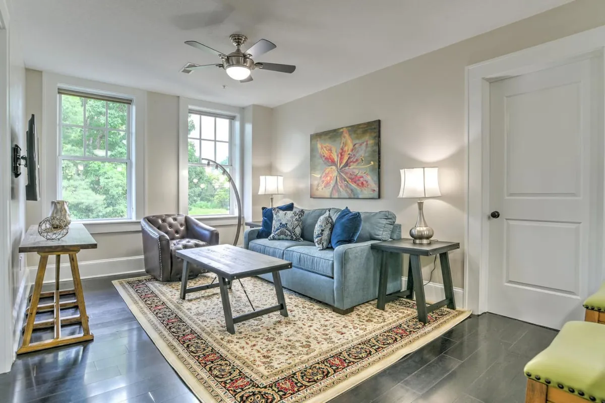 A cozy interior scene centered around a blue couch paired with framed artwork, illuminated by table lamps and set atop an oriental rug. The arrangement invites relaxation, reading, or socializing in a stylish, comfortable setting.