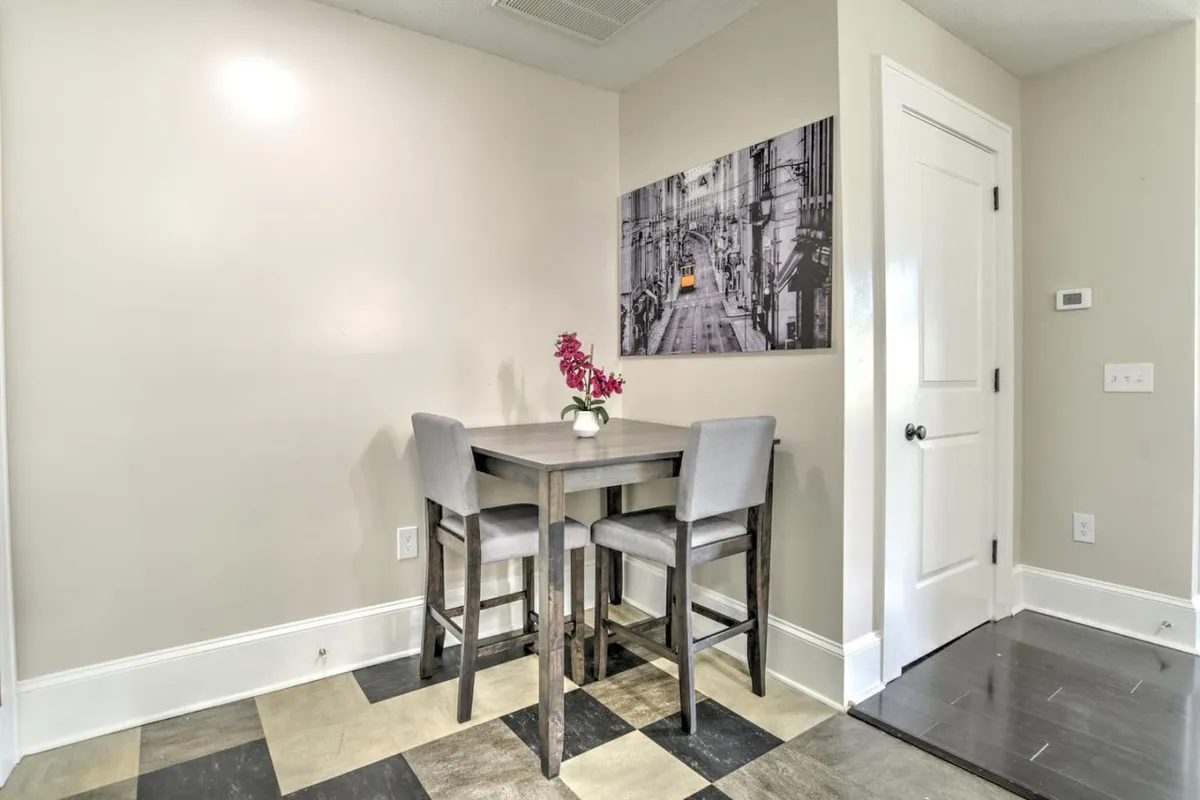A cozy interior scene featuring a small dining table set with two chairs. The table is adorned with a flower vase, and tasteful wall art hangs nearby, creating an inviting space perfect for casual dining or sharing a morning coffee.